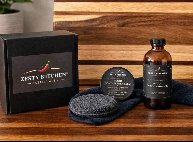 Zesty Kitchen products including a bottle, balm, and packaging on a wooden surface with a cutting board in the background.